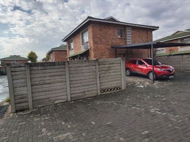 Exterior view of a face brick townhouse featuring a paved driveway, carport, and precast concrete boundary wall within a residential complex.