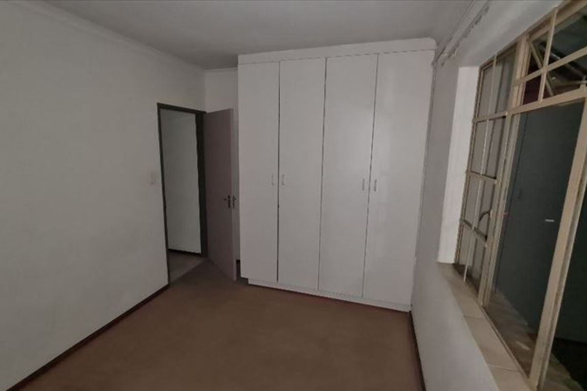 An empty bedroom featuring built-in white cupboards and metal-framed windows, requiring cosmetic updates to flooring and paintwork.