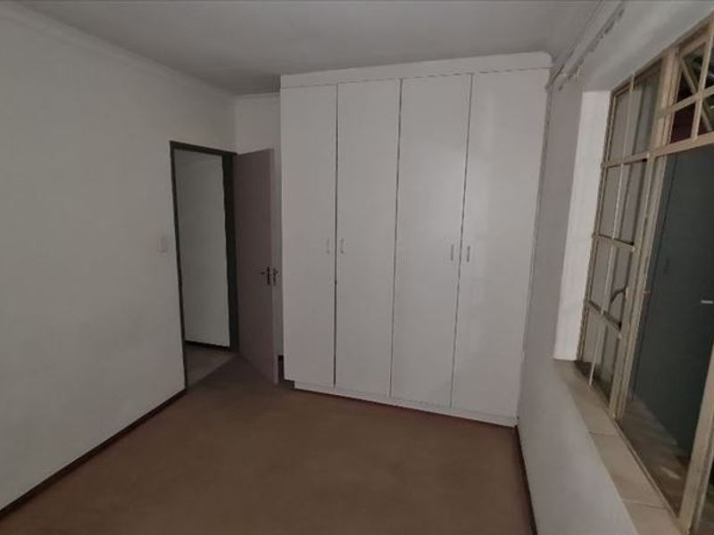 An empty bedroom featuring built-in white cupboards and metal-framed windows, requiring cosmetic updates to flooring and paintwork.