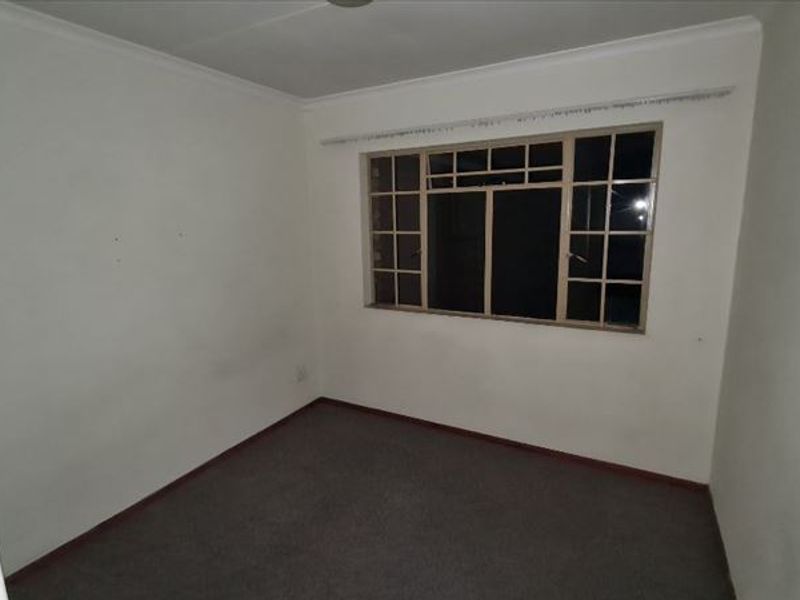 An empty bedroom featuring a grid-pattern window, carpeted flooring, and coved ceilings, ready for a fresh update.