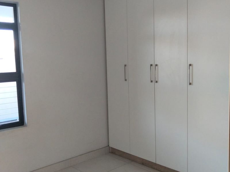 A clean, empty bedroom featuring modern white built-in cupboards, neutral tiled flooring, and a contemporary aluminium window frame.