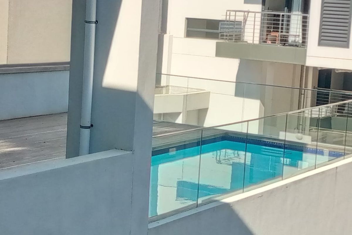 An elevated view of a swimming pool area featuring modern glass balustrades and timber decking within an apartment complex.