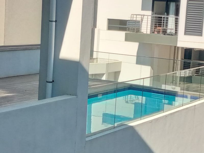 An elevated view of a swimming pool area featuring modern glass balustrades and timber decking within an apartment complex.