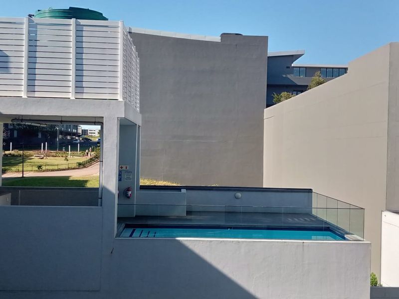 An elevated view of a modern swimming pool area featuring a glass balustrade and a water tank structure within an apartment complex.