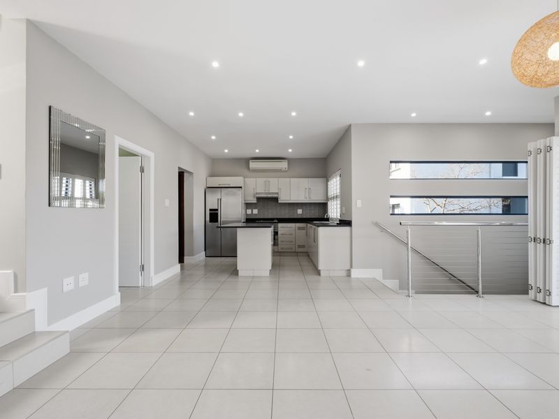 Spacious open-plan living area featuring a modern kitchen with island, tiled flooring, recessed lighting, and a staircase with stainless steel balustrade.