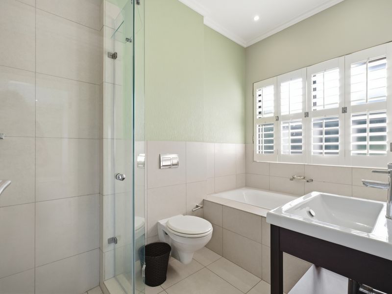 Modern bathroom featuring a glass-enclosed shower, built-in bathtub, wall-mounted toilet, and a basin with contemporary fixtures, complemented by plantation shutters.
