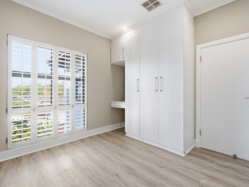 Bright bedroom featuring built-in cupboards, a integrated desk, plantation shutters, and modern laminate flooring.
