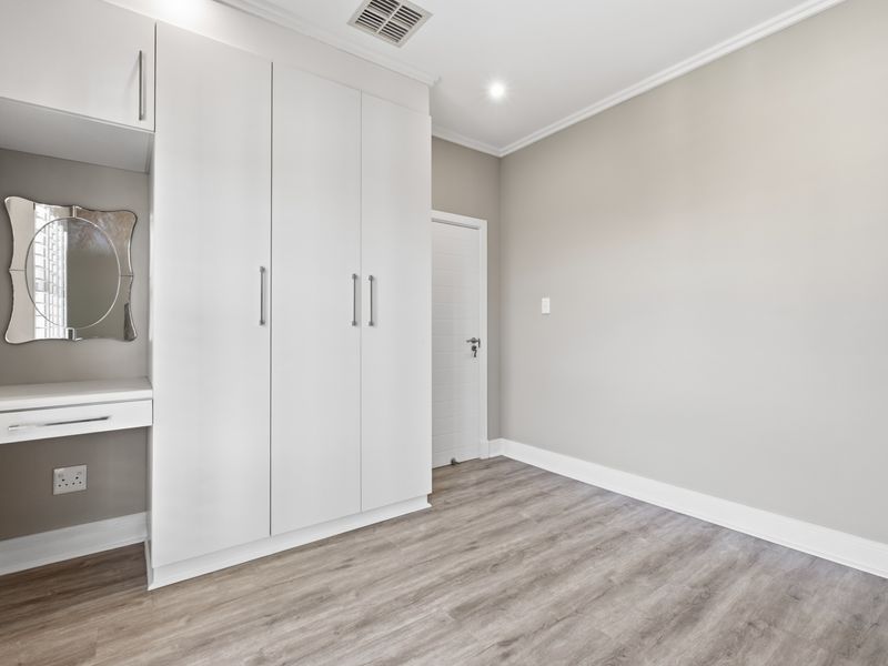 A clean, modern bedroom featuring light laminate flooring, neutral walls, and a built-in wardrobe with an integrated vanity station.