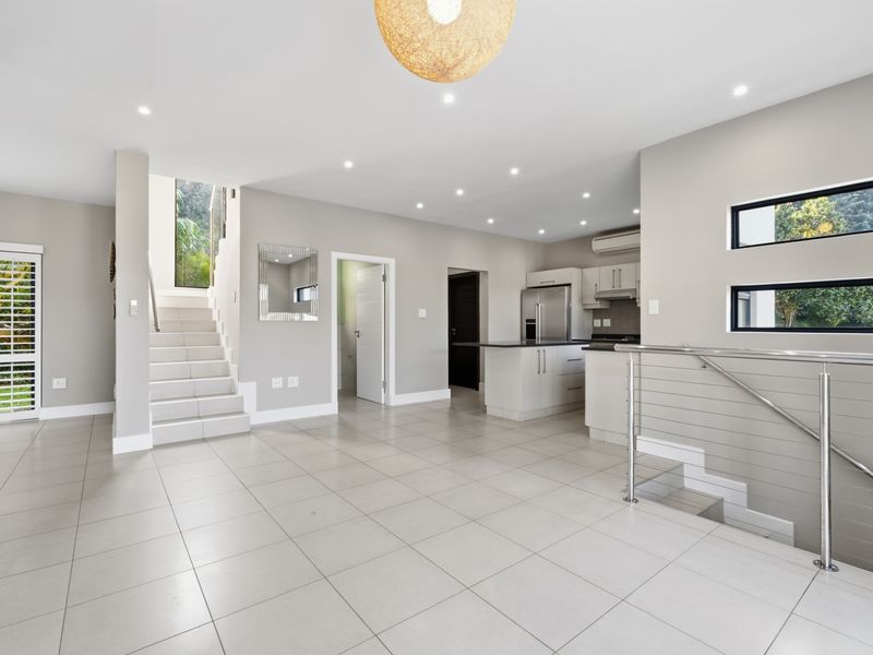 Spacious open-plan living area featuring tiled floors, recessed lighting, a modern kitchen with island, and a staircase with a sleek stainless steel balustrade.