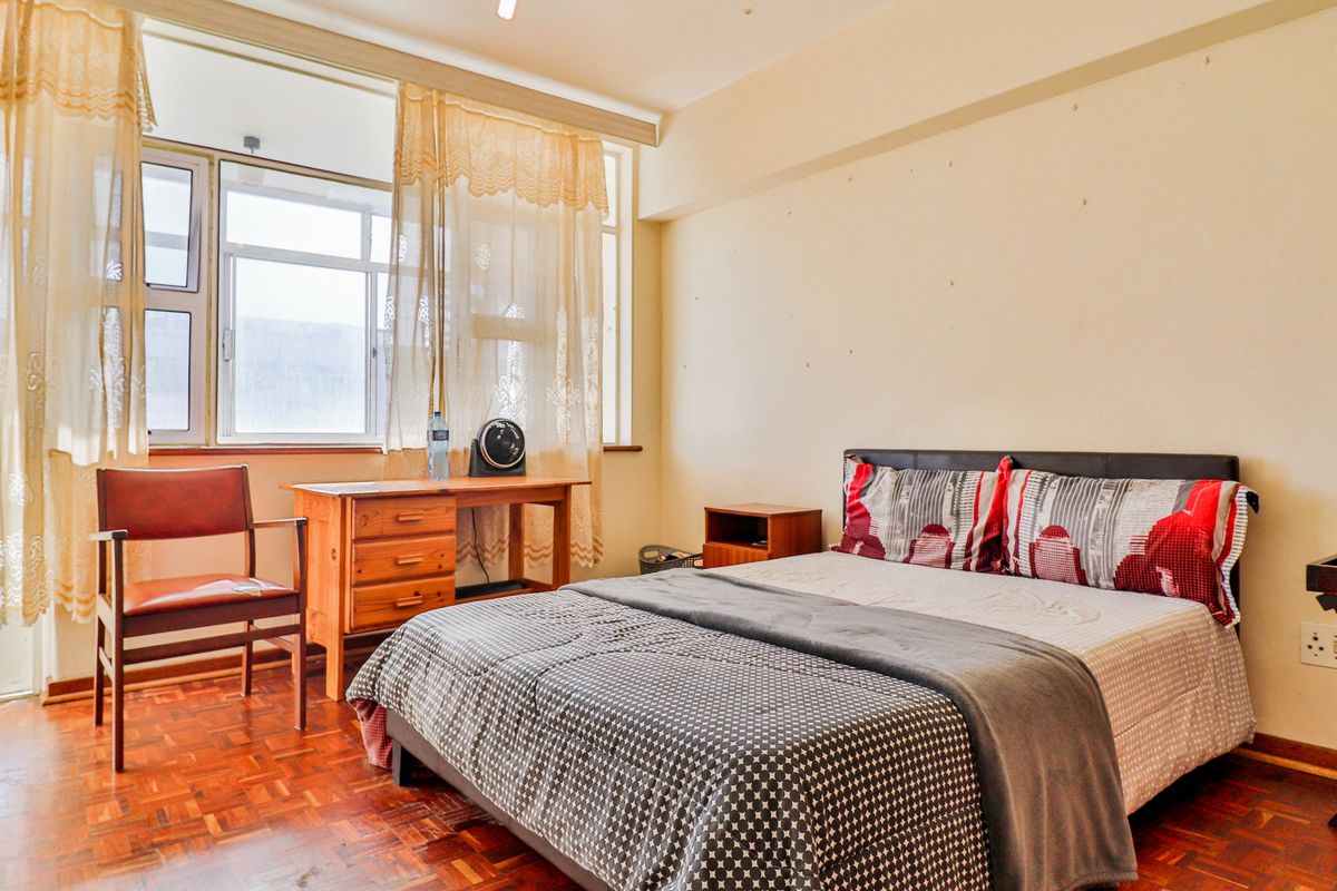 A bedroom featuring parquet flooring and a large window, requiring cosmetic updates to the wall surfaces to improve the overall aesthetic.