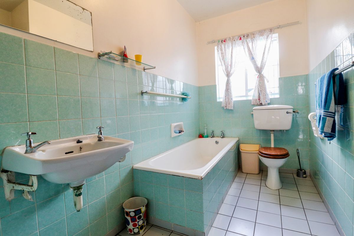 A dated bathroom featuring light blue wall tiling, a standard bathtub, pedestal basin, and white floor tiles, offering potential for a modern renovation.