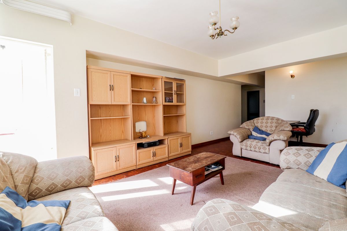 Spacious living room featuring parquet flooring and built-in wooden cabinetry, offering a functional layout with natural light.