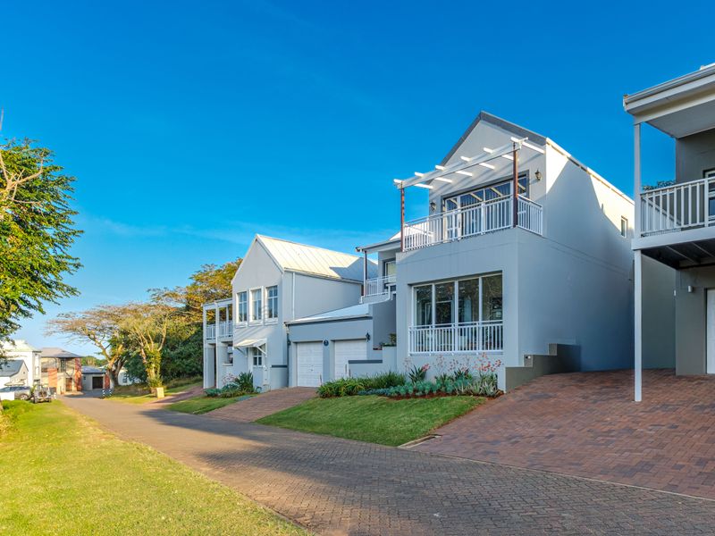 Modern multi-story residential property featuring a paved driveway, double garage, and an upper-level balcony with a pergola.