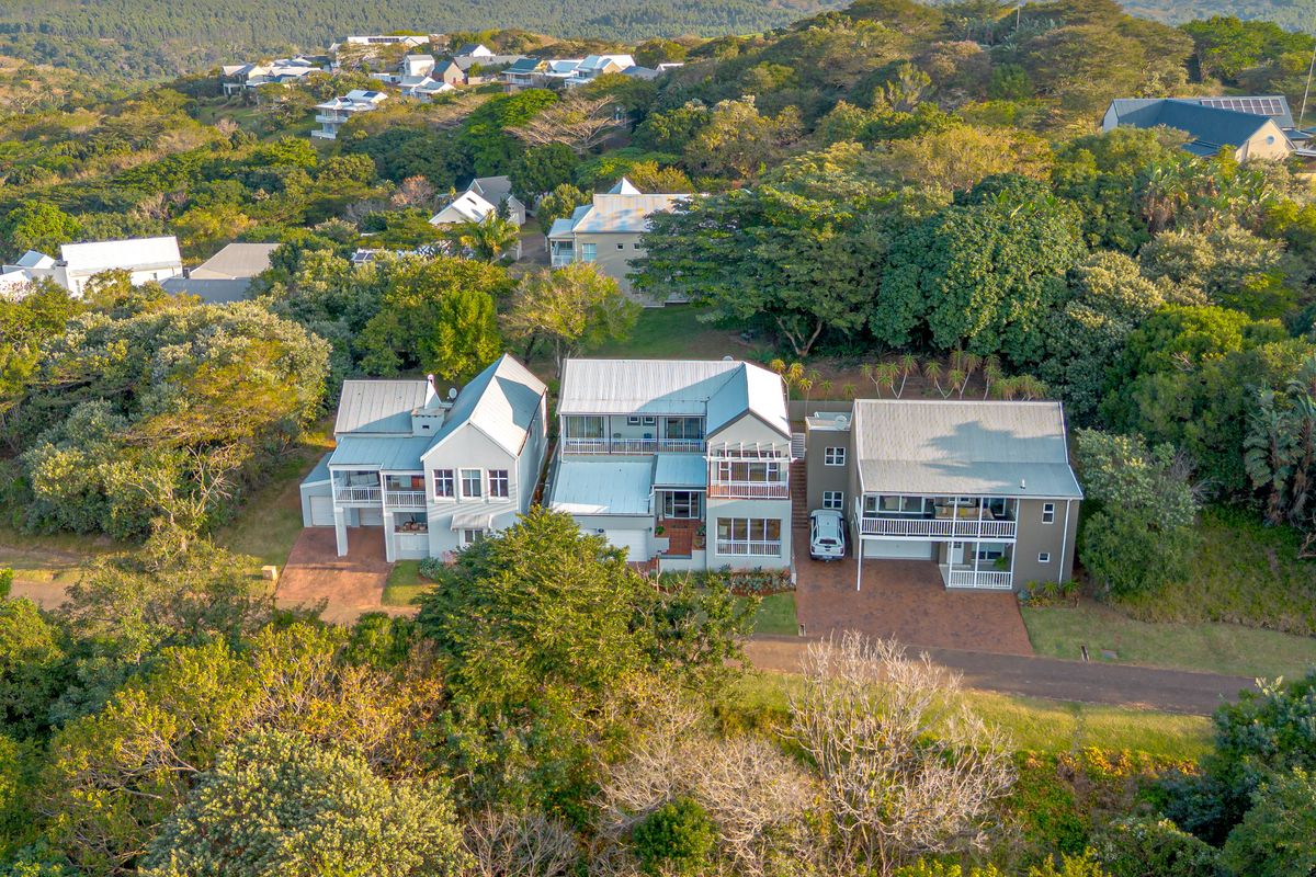 Aerial view of a residential property complex featuring multi-level homes with metal roofing, balconies, and paved driveways set within a lush, wooded estate.