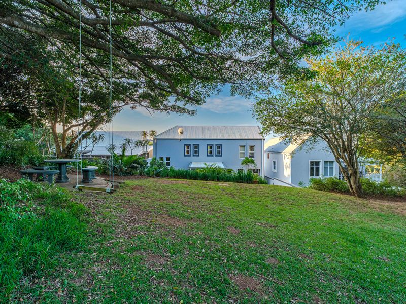 A spacious rear garden featuring a well-maintained lawn and mature trees, providing a scenic view of the property's rear elevation and metal roof structure.