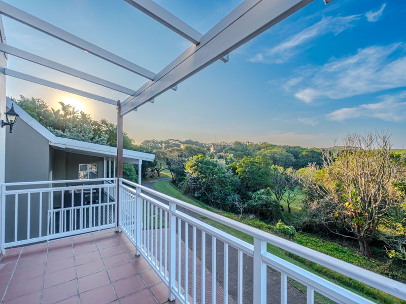A spacious balcony featuring tiled flooring, a white metal railing, and a pergola structure, offering scenic views of the surrounding greenery.