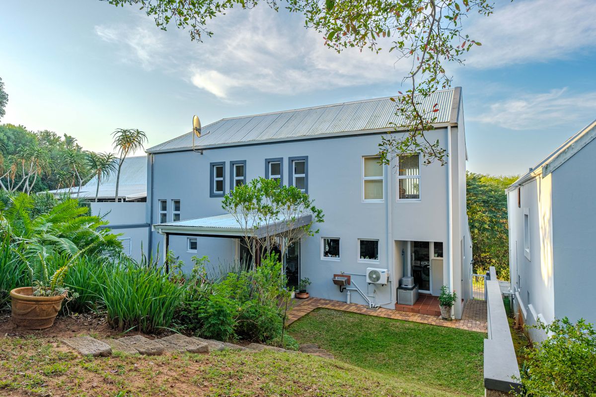 Rear view of a two-story residential property featuring a corrugated metal roof, paved patio area, and established garden landscaping.