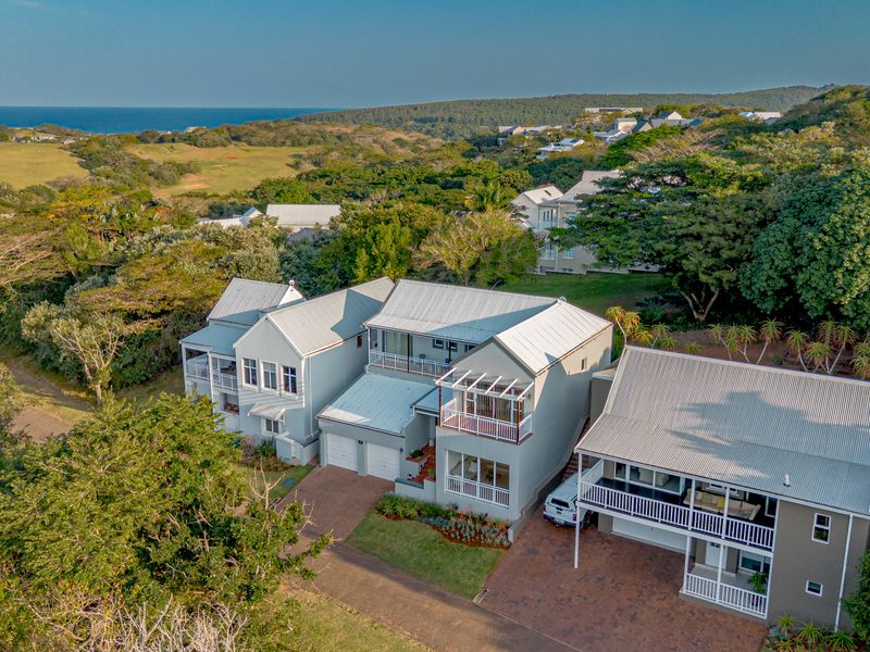 Aerial view of a multi-level residential property featuring metal roofing, paved driveways, and balconies, set within a landscaped coastal estate.