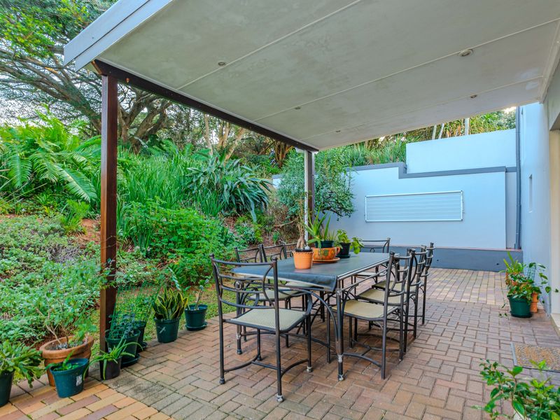 A covered outdoor patio area featuring brick paving and recessed lighting, overlooking a landscaped garden with a retaining wall.