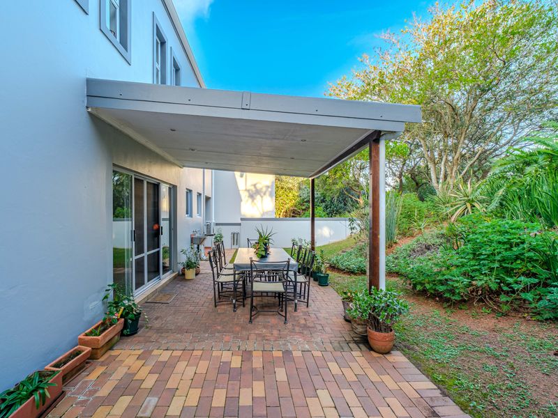 A covered outdoor patio area featuring brick paving, direct access to the home via sliding glass doors, and views of the surrounding garden.