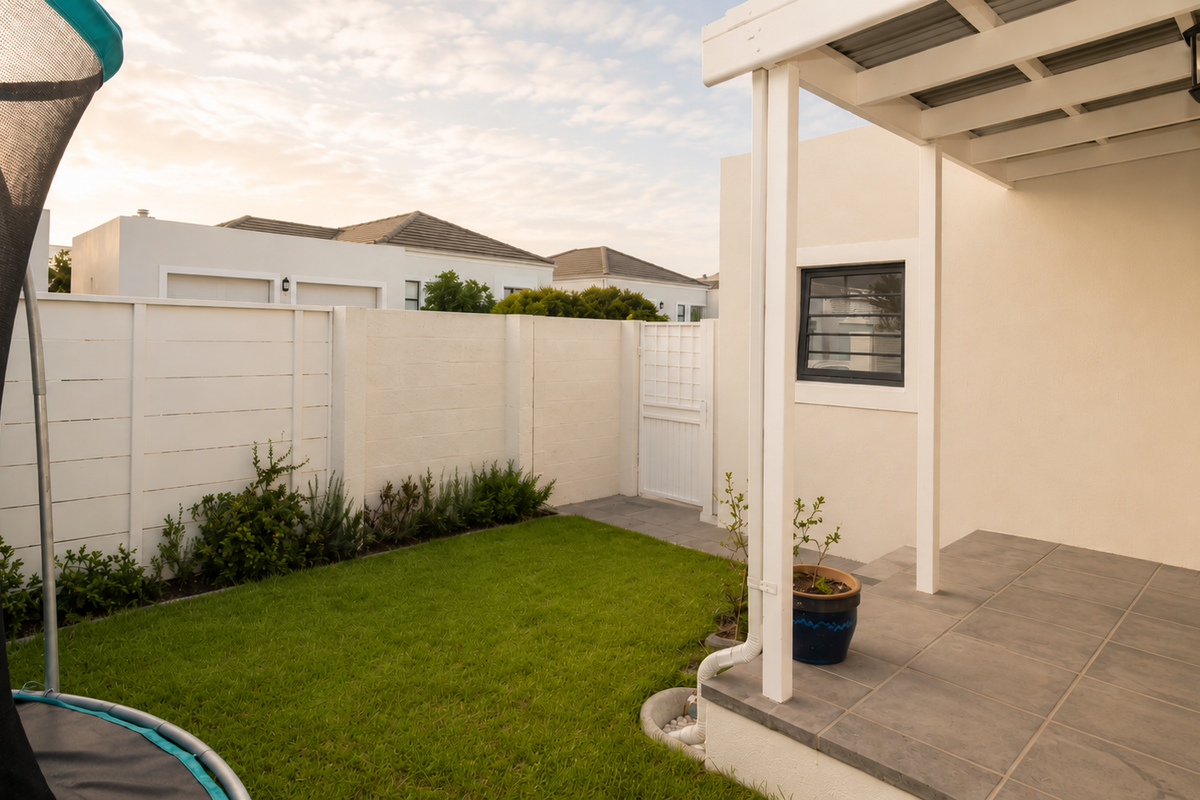 A neat rear garden featuring a tiled patio with a covered pergola, enclosed by a secure boundary wall and a small lawn area.