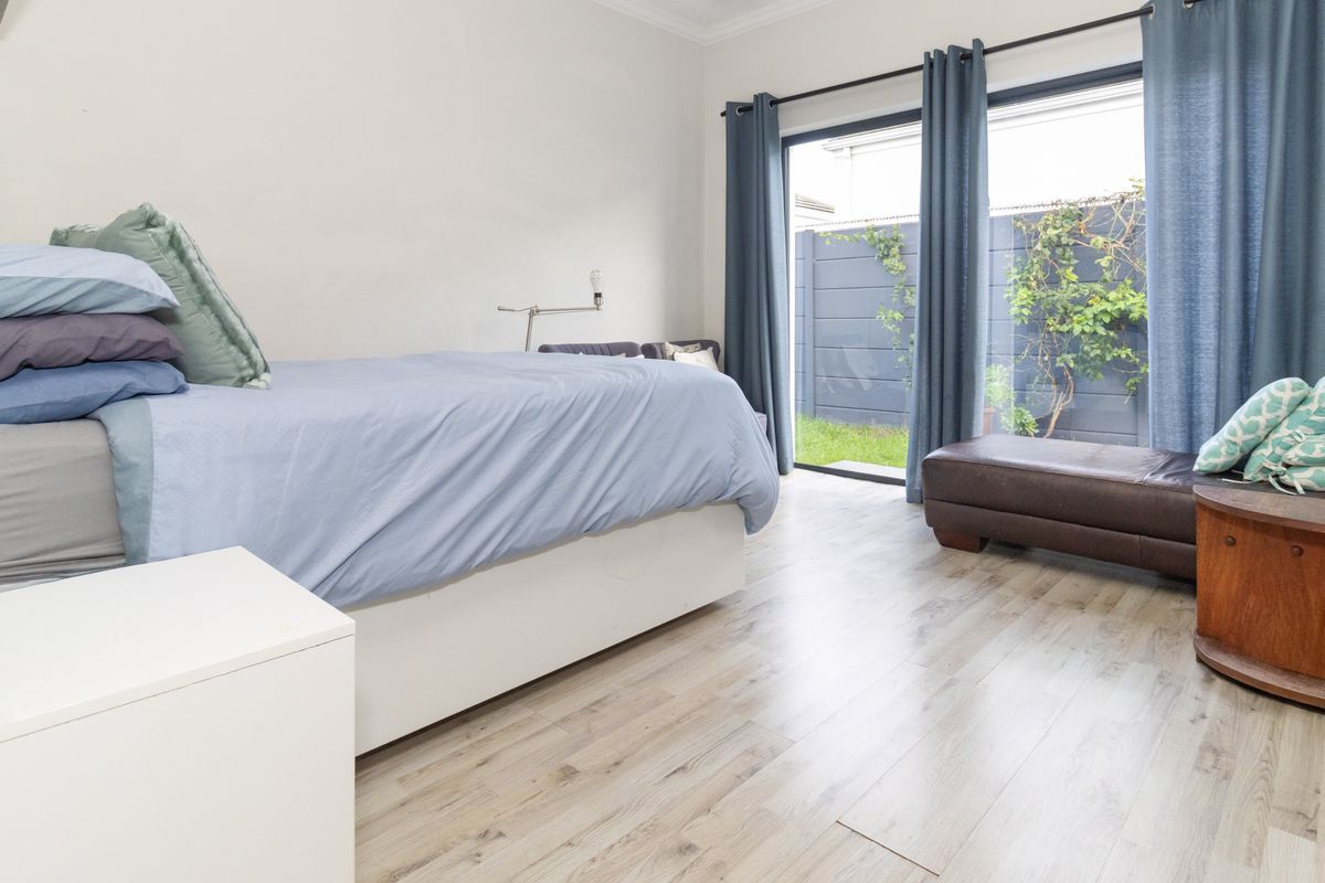 A bright bedroom featuring light-toned laminate flooring and a large sliding glass door providing direct access to the rear garden area.