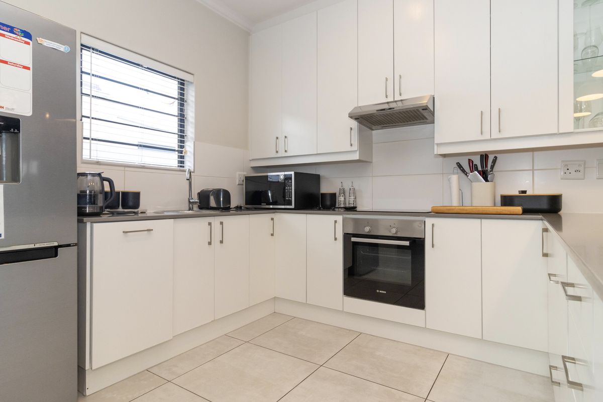 A clean, modern kitchen featuring white cabinetry, tiled backsplash, stainless steel oven, extractor fan, and neutral floor tiles.