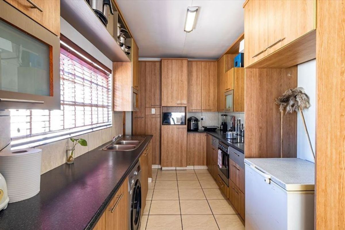 A functional galley-style kitchen featuring wood-finish cabinetry, laminate countertops, a built-in oven, and tiled flooring with ample storage space.