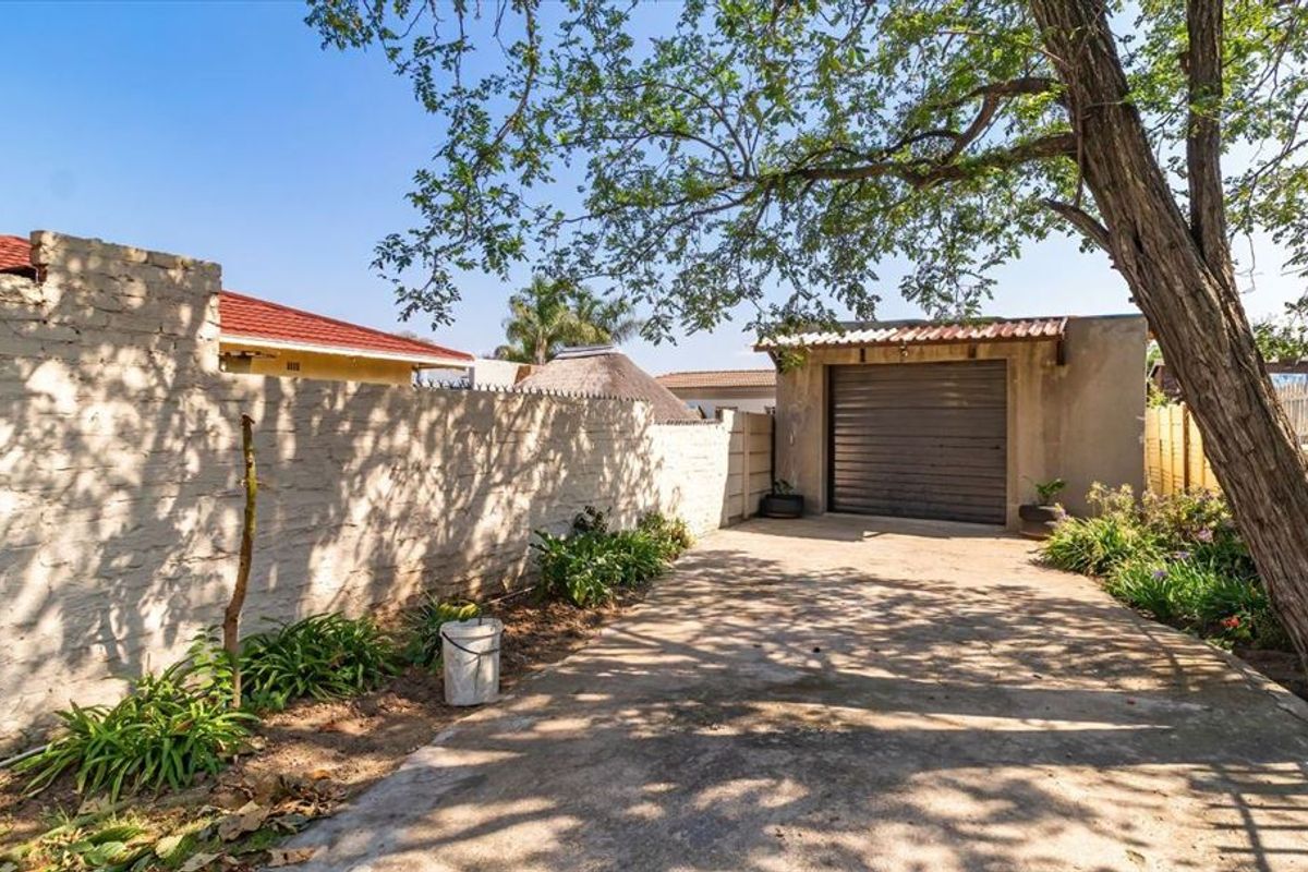 Rear exterior view featuring a concrete driveway, a detached garage with a metal door, and a perimeter boundary wall.