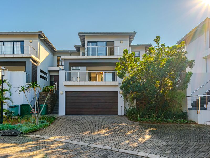 Front elevation of a modern townhouse featuring a paved driveway, double garage, and upper-level balconies with glass railings.