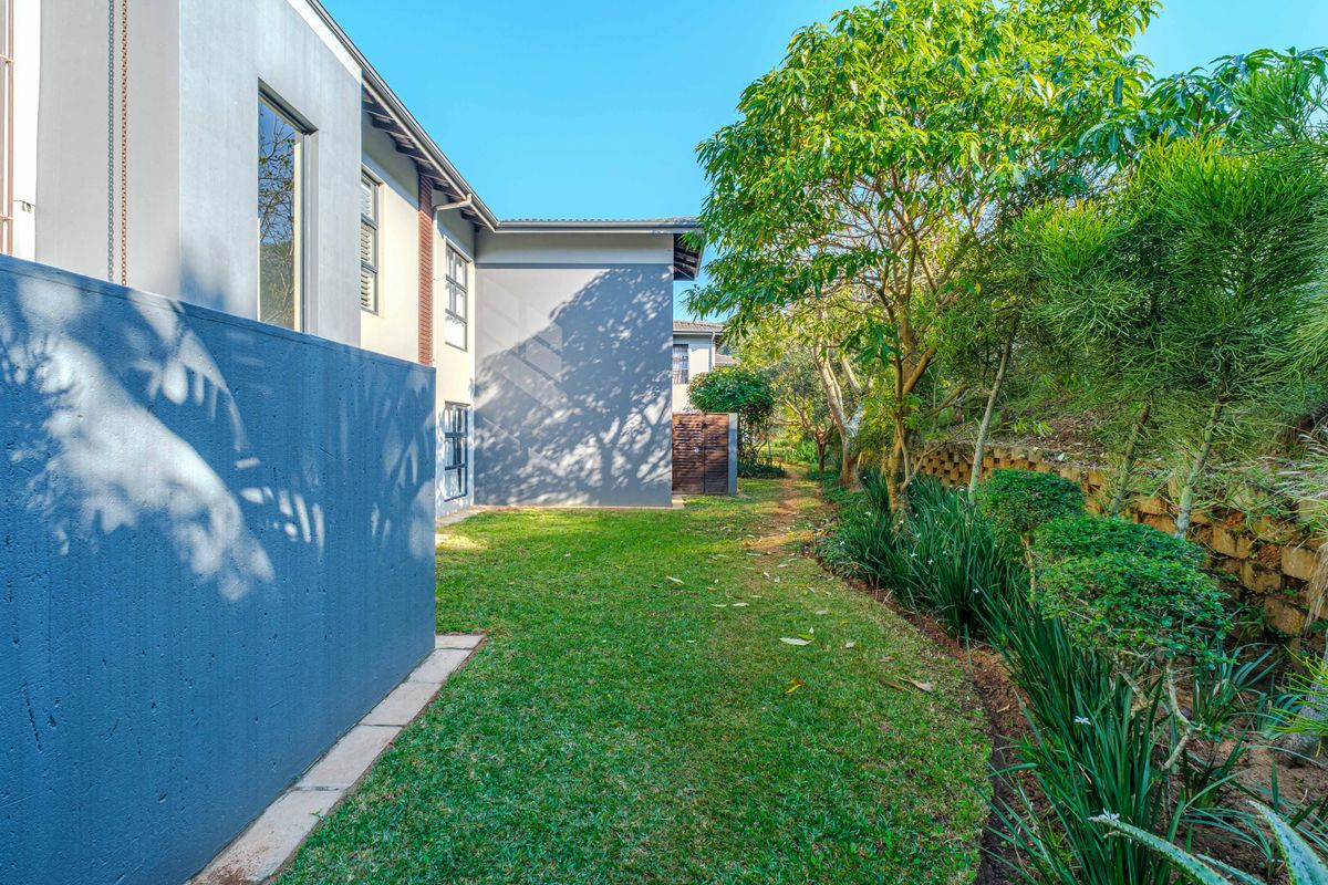 A well-maintained rear garden area featuring a lush lawn, established trees, and a concrete boundary wall adjacent to the townhouse structure.