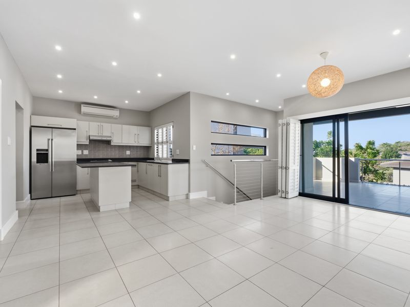 Spacious open-plan living and kitchen area featuring modern cabinetry, tiled floors, recessed lighting, and large sliding doors leading to an outdoor balcony.