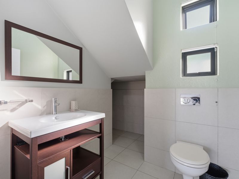 Modern bathroom featuring a vanity cabinet with basin, wall-hung toilet with concealed cistern, and tiled finishes under a sloped ceiling.