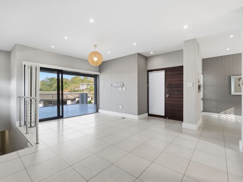 Spacious, light-filled living area featuring neutral tiled flooring, modern recessed lighting, and large sliding doors opening onto an outdoor balcony.