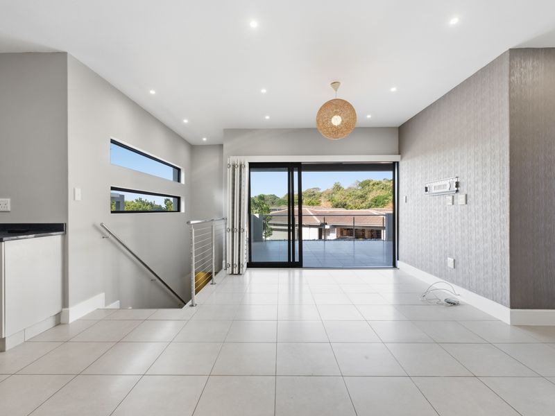 Spacious open-plan living area featuring modern tiled floors, recessed lighting, a textured feature wall, and large sliding doors opening to an outdoor balcony.