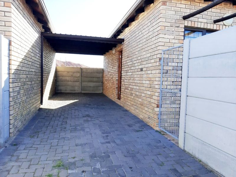 A paved driveway area featuring a covered carport structure, enclosed by brick walls and a precast concrete boundary fence with a metal security gate.