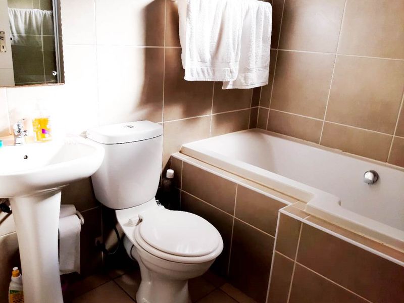A functional bathroom featuring a pedestal basin, a standard toilet, and a built-in bathtub with neutral wall and floor tiling.