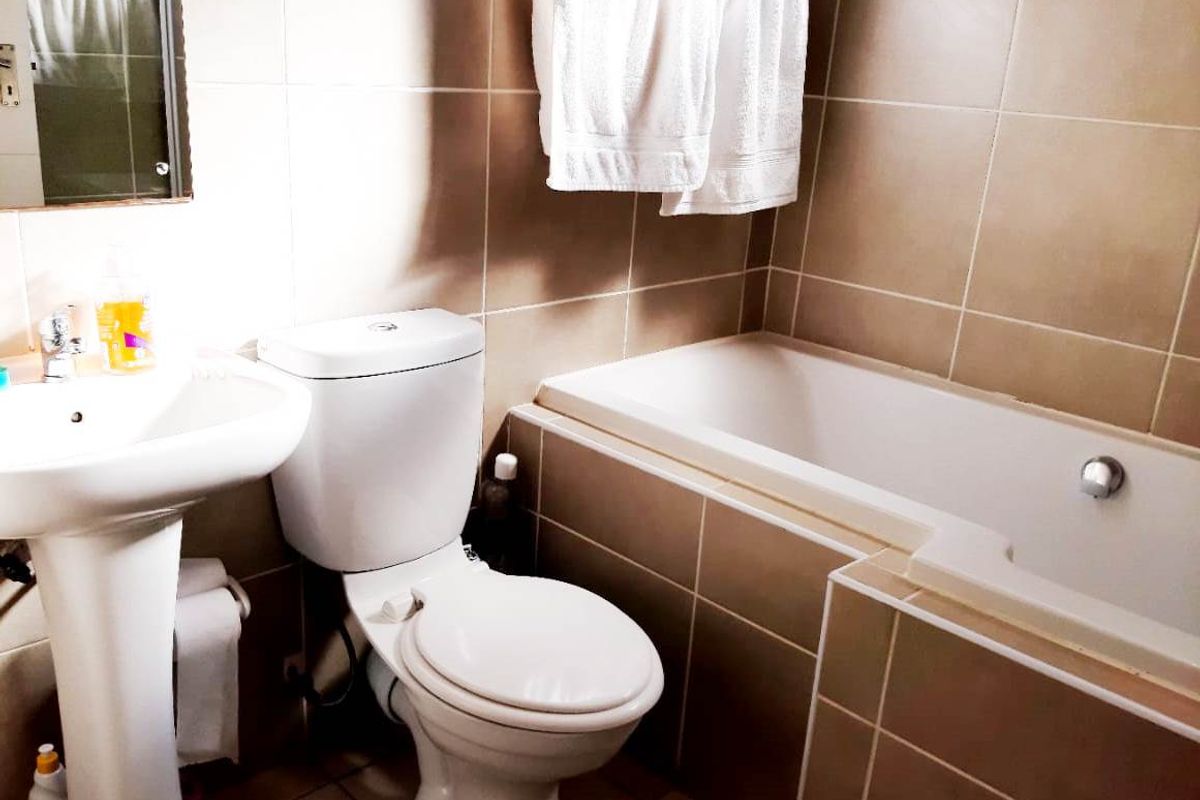 A functional bathroom featuring a pedestal basin, a standard toilet, and a built-in bathtub with neutral wall and floor tiling.