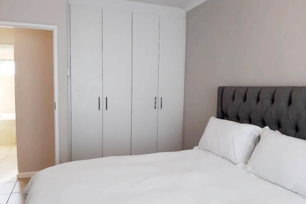 A well-maintained bedroom featuring built-in cupboards and neutral wall finishes, with direct access to an adjoining bathroom.