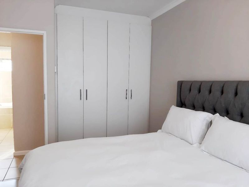 A well-maintained bedroom featuring built-in cupboards and neutral wall finishes, with direct access to an adjoining bathroom.