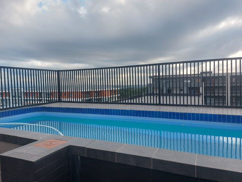 An elevated outdoor swimming pool featuring tiled coping and a secure metal safety railing, offering views of the surrounding apartment complex.