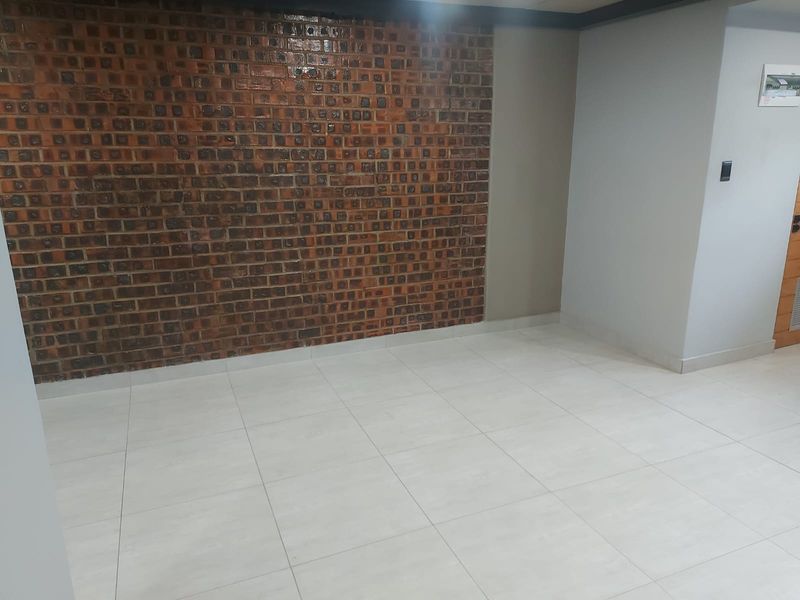 An empty living area featuring a prominent exposed brick feature wall and neutral ceramic floor tiles, providing a clean and versatile space.