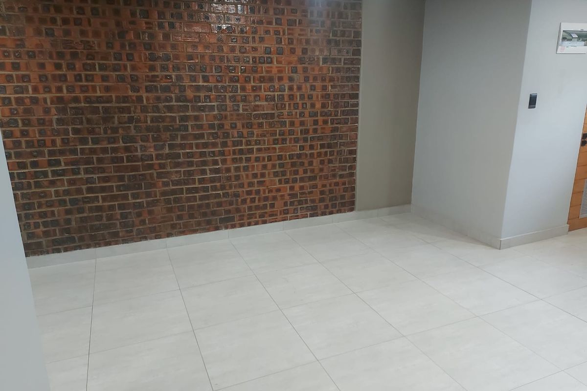 An empty living area featuring a prominent exposed brick feature wall and neutral ceramic floor tiles, providing a clean and versatile space.
