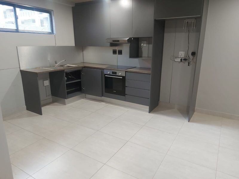 Modern kitchen featuring dark grey cabinetry, integrated oven and hob, stainless steel sink, and tiled flooring in an open-plan layout.