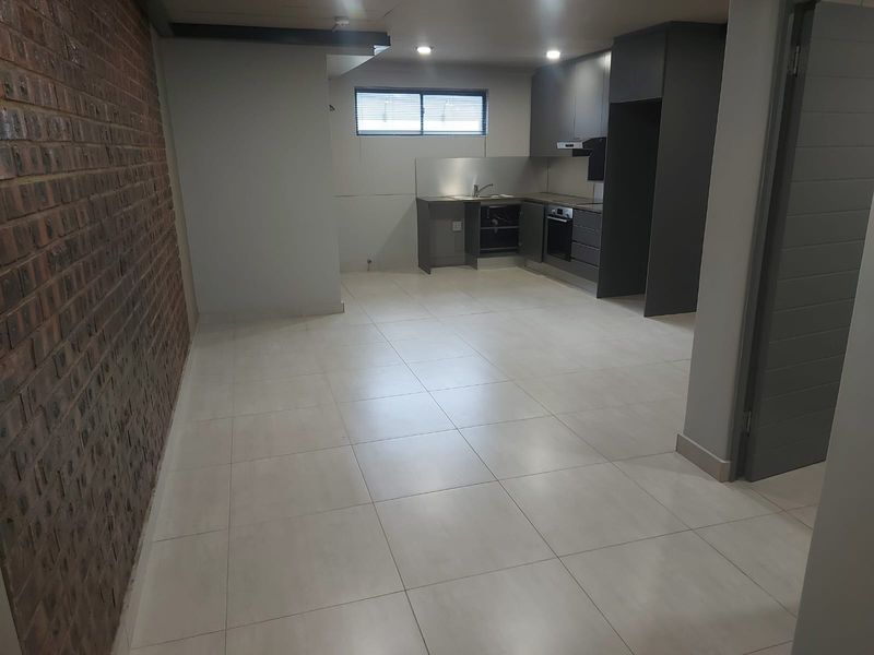 Open-plan living and kitchen area featuring tiled floors, an exposed brick feature wall, and modern dark cabinetry with integrated oven and extractor.