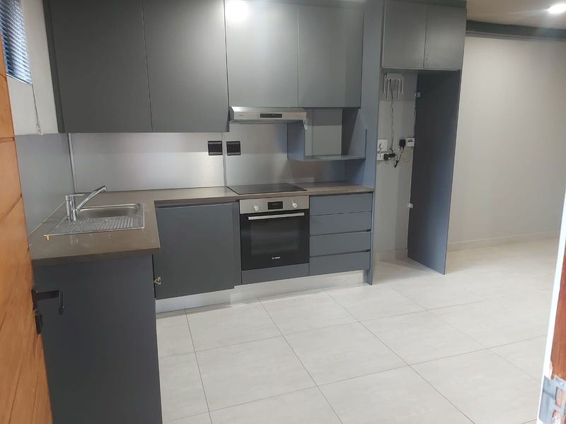 Modern kitchen featuring dark grey cabinetry, integrated oven and hob, stainless steel sink, and tiled flooring in an open-plan layout.
