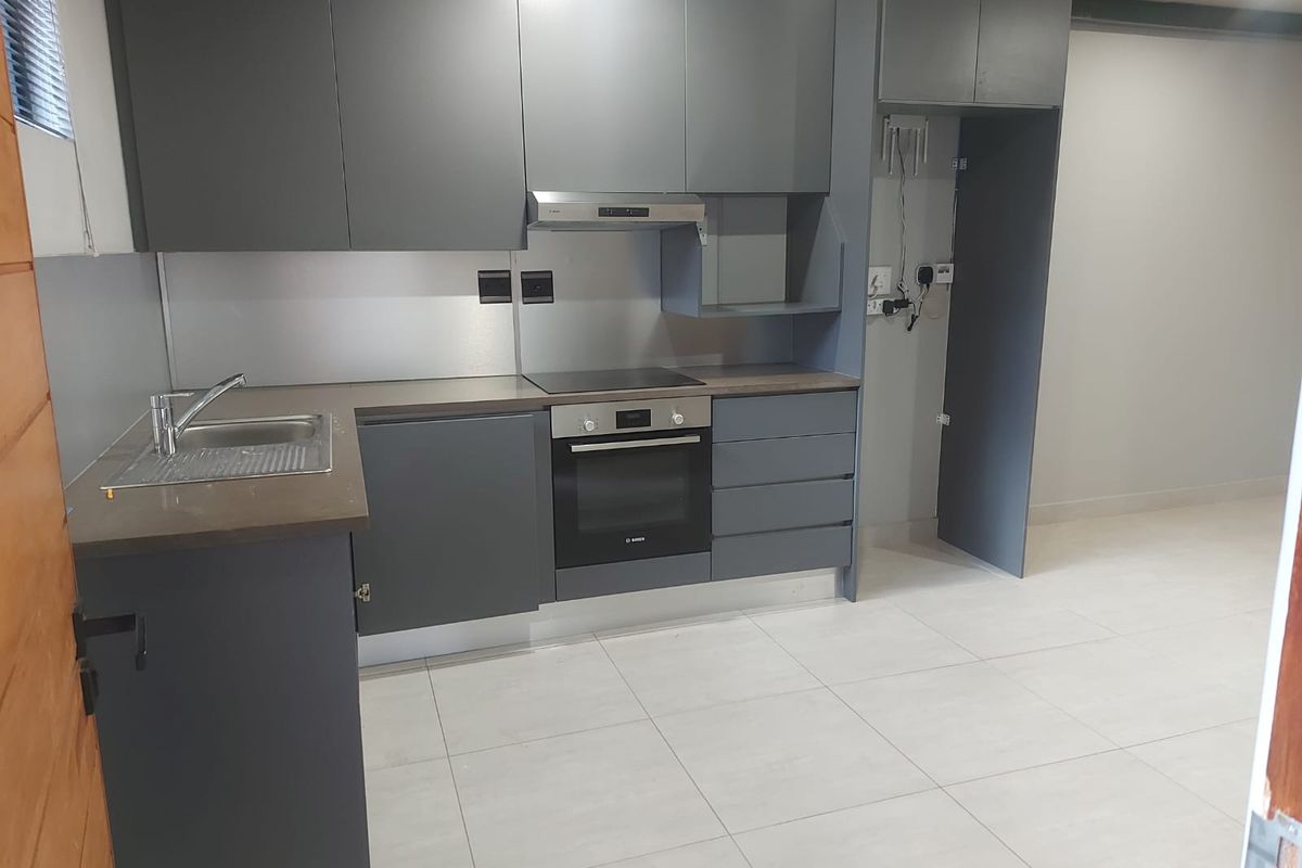 Modern kitchen featuring dark grey cabinetry, integrated oven and hob, stainless steel sink, and tiled flooring in an open-plan layout.