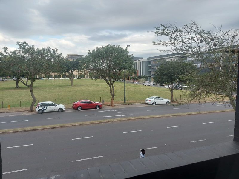 An elevated view overlooking a public road, green space, and surrounding urban development.