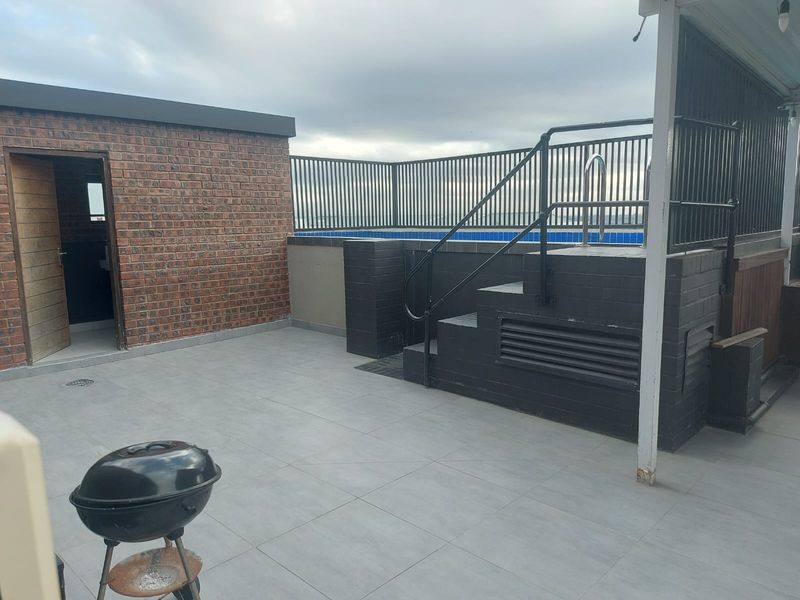 An outdoor rooftop terrace featuring a raised swimming pool with metal safety railings, tiled flooring, and a brick-walled utility structure.