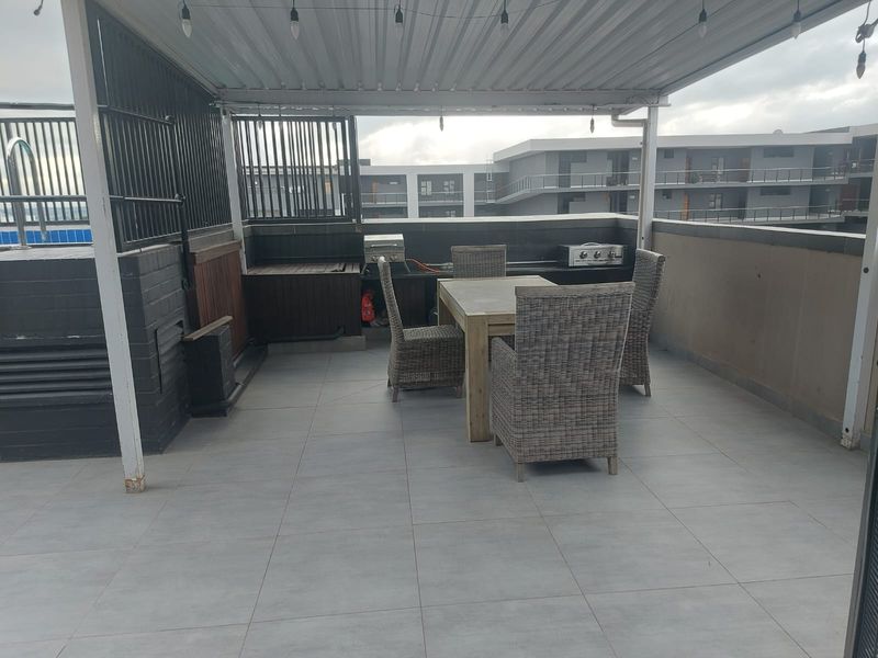 A covered outdoor patio featuring tiled flooring, a built-in braai area, and a metal roof structure, ideal for outdoor dining and entertainment.